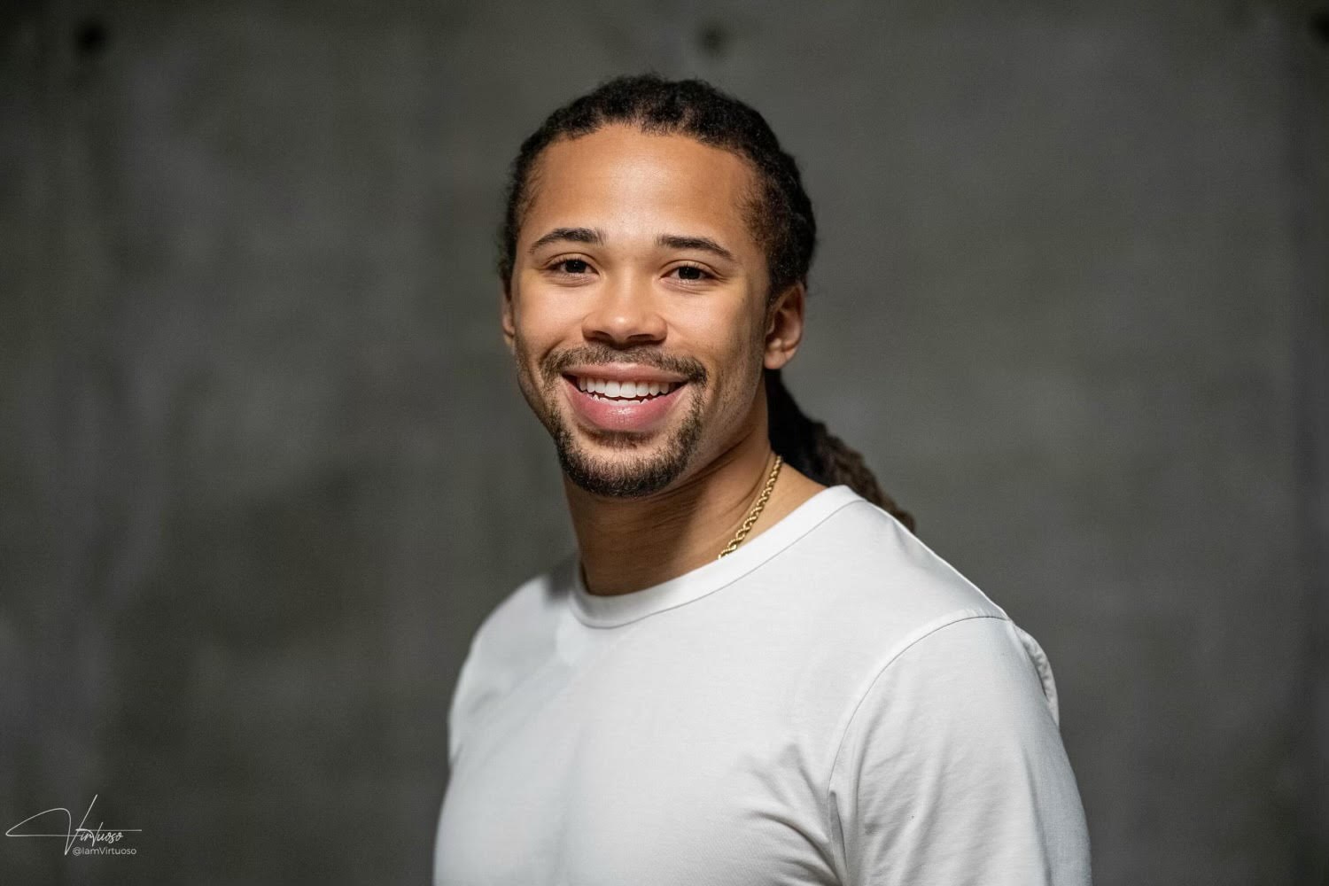 Hezi Ross, photographed against a grey wall, smiling, in a white t-shirt.